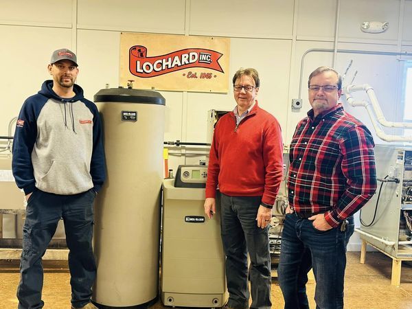 Three men stand in front of air conditioning equipment with "Lochard Inc" sign on wall